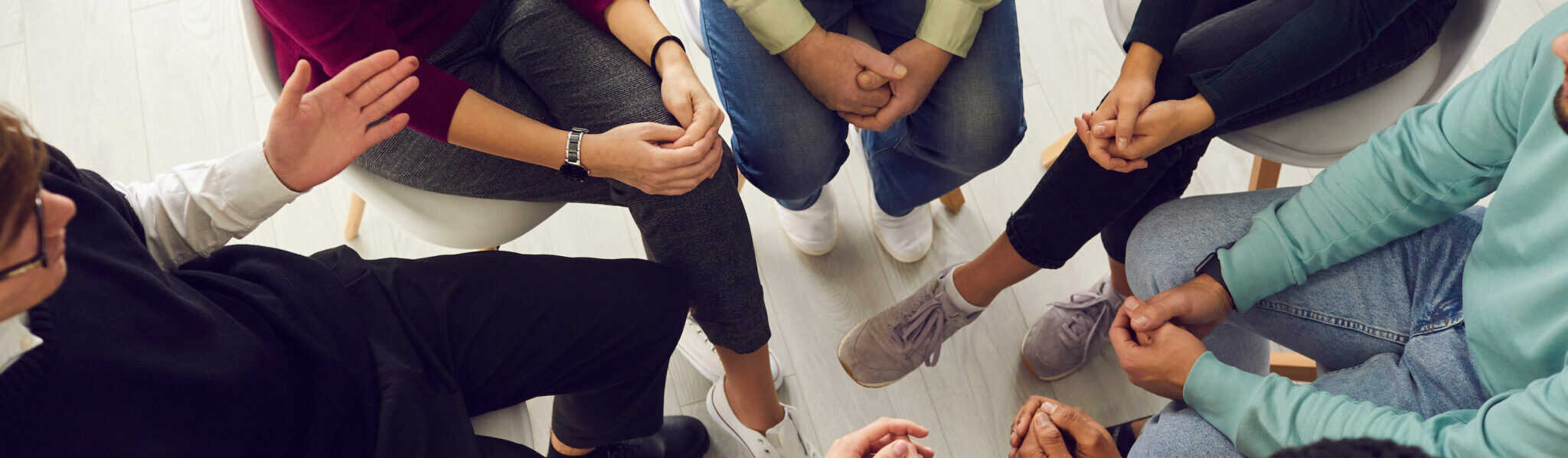 Top view of diverse people sitting in a close circle and talking to a therapist. Cropped image of unidentified people receive help and support during a group therapy session. Concept of group therapy.